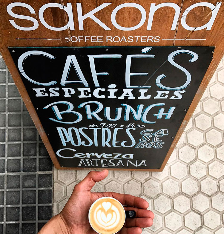 Mano sujetando un café con cartel de la cafetería Sakona